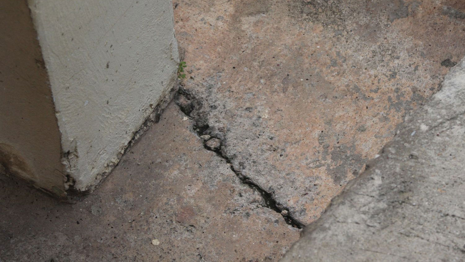 Cracked concrete floor near a foundation wall with visible separation and surface damage.