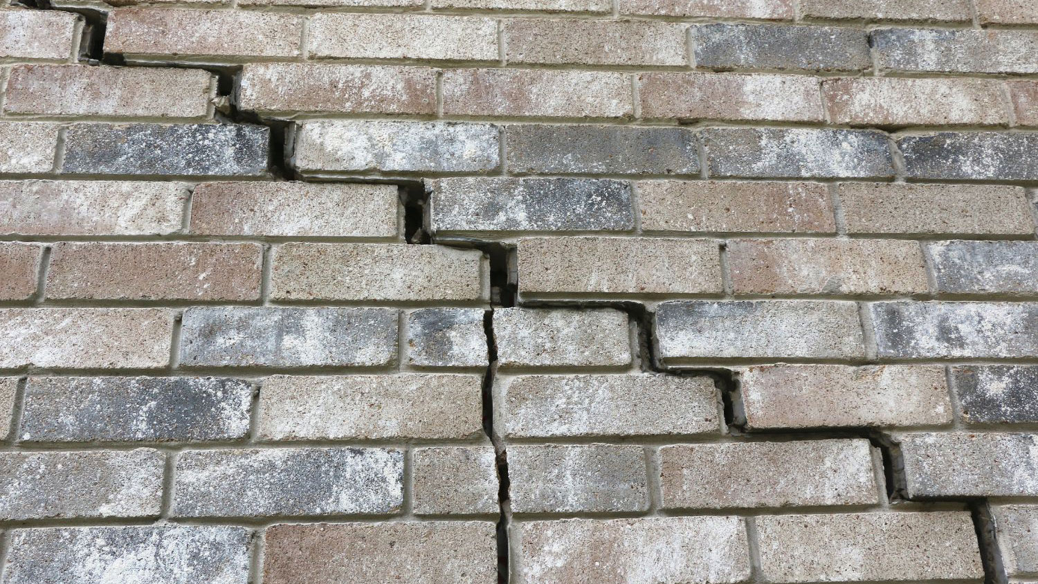 Brick foundation wall showing extensive horizontal and vertical cracks with visible mortar separation and shifting bricks.