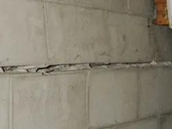 Concrete block foundation wall showing a long horizontal crack along the mortar joint.
