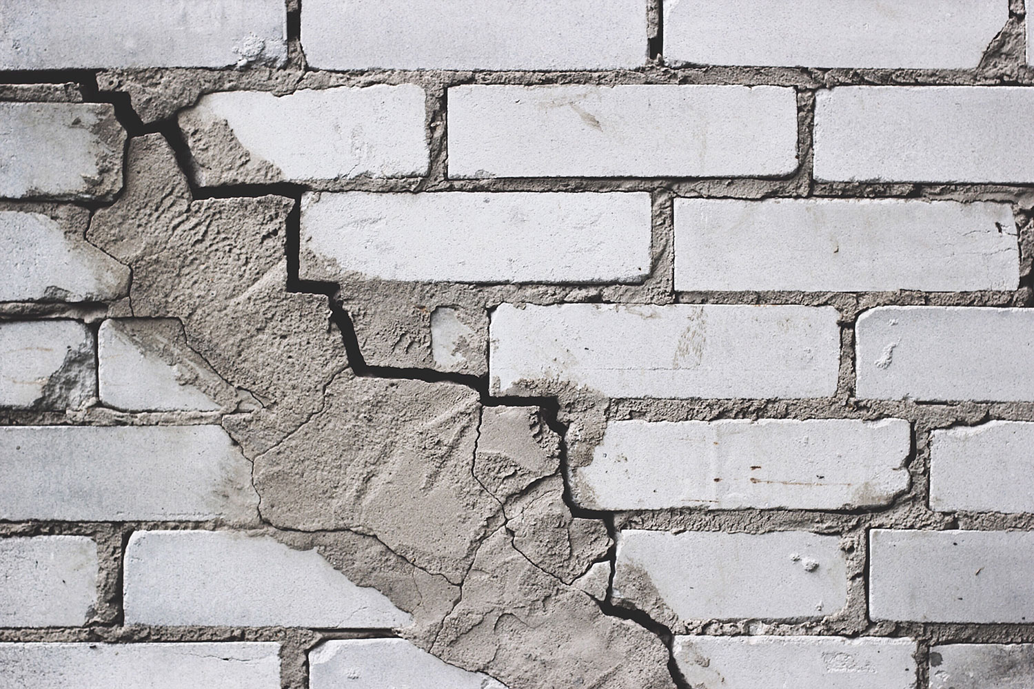 Severely damaged brick wall with large cracks, crumbling mortar, and displaced bricks.